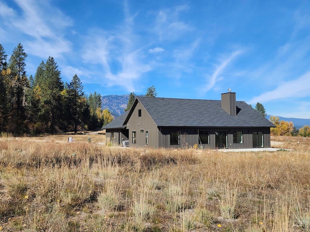 rear view of property with roof with shingles, a mountain view, and a chimney