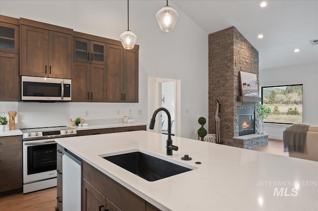 kitchen with appliances with stainless steel finishes, light countertops, a sink, and a stone fireplace