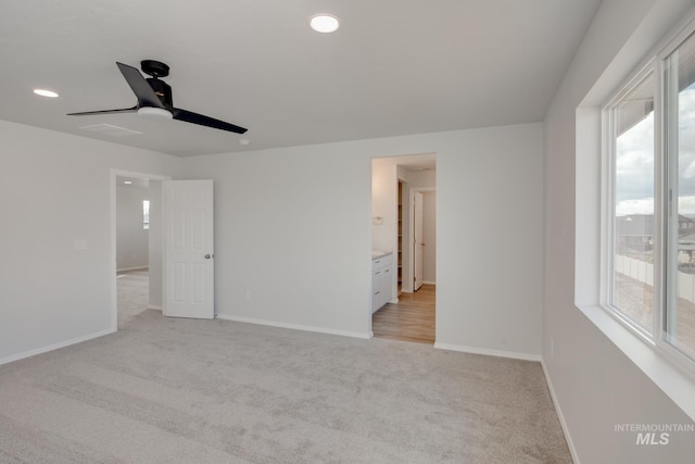 unfurnished bedroom featuring ceiling fan, light colored carpet, and ensuite bath