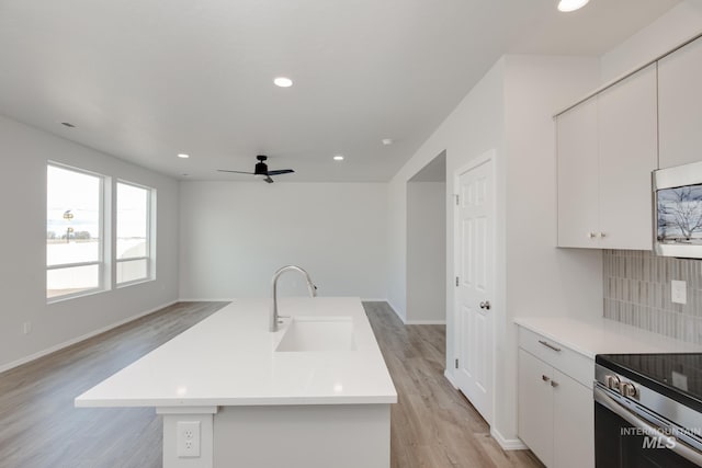 kitchen featuring sink, backsplash, an island with sink, white cabinets, and light wood-type flooring