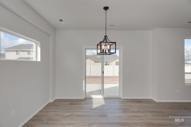 unfurnished dining area with a chandelier, plenty of natural light, and light hardwood / wood-style floors