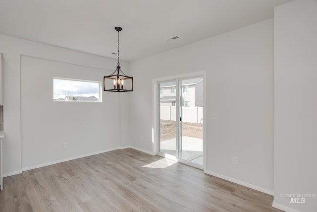 unfurnished room with a healthy amount of sunlight, light wood-type flooring, and an inviting chandelier