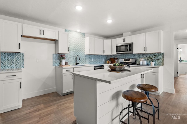 kitchen featuring a breakfast bar, a sink, stainless steel appliances, white cabinets, and light wood-type flooring