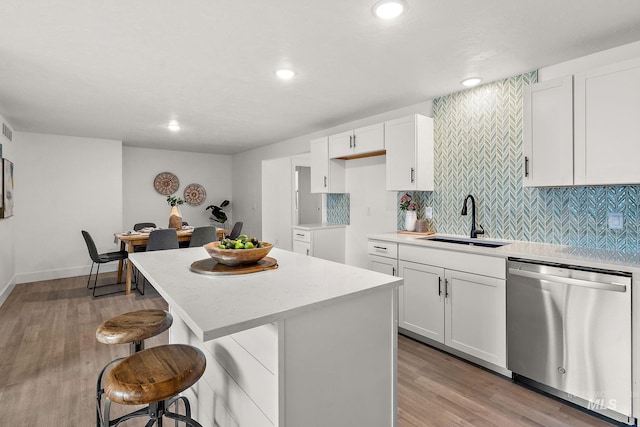 kitchen featuring light wood-style flooring, a sink, stainless steel dishwasher, a kitchen breakfast bar, and tasteful backsplash