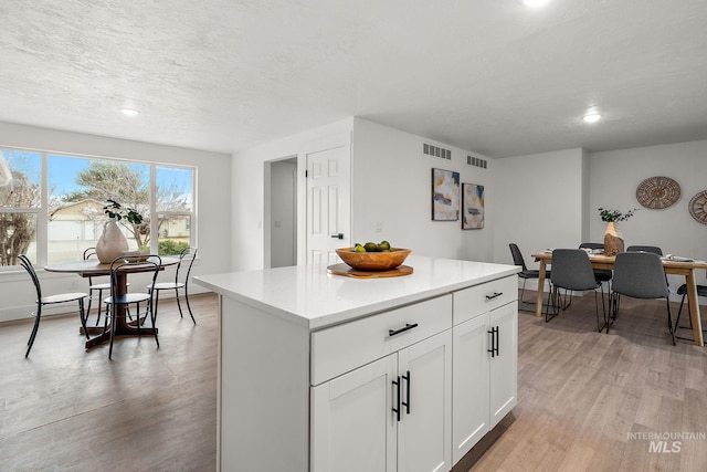 kitchen with visible vents, a center island, light countertops, light wood-type flooring, and white cabinets