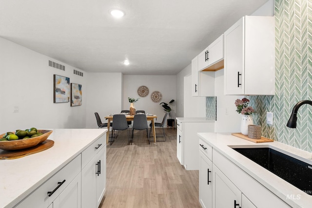 kitchen featuring tasteful backsplash, visible vents, light wood-style flooring, and a sink