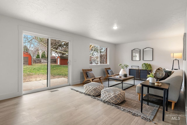 living area featuring visible vents, a textured ceiling, baseboards, and wood finished floors