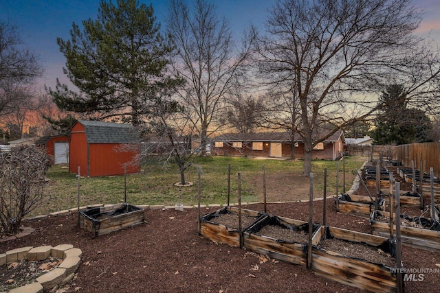 yard at dusk featuring an outbuilding, fence, a storage shed, and a garden