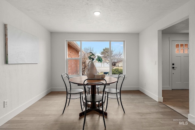 dining room featuring a textured ceiling, baseboards, and light wood-style floors