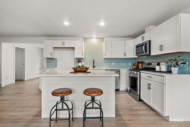 kitchen featuring a breakfast bar, light wood-style flooring, a kitchen island, stainless steel appliances, and decorative backsplash