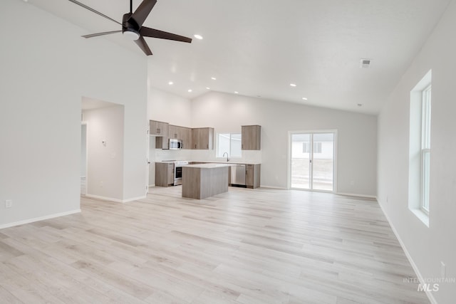 unfurnished living room with baseboards, light wood-style floors, high vaulted ceiling, a ceiling fan, and a sink