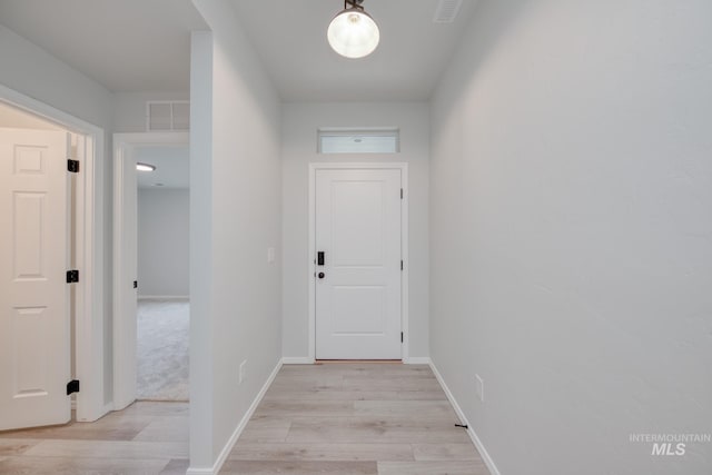 hall with visible vents, baseboards, and light wood finished floors