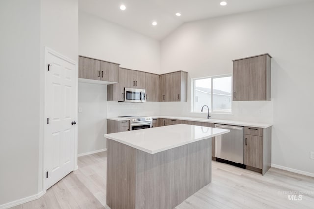 kitchen with high vaulted ceiling, modern cabinets, a sink, stainless steel appliances, and light wood finished floors