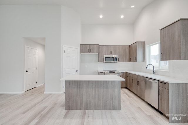 kitchen with a sink, a center island, a towering ceiling, stainless steel appliances, and modern cabinets