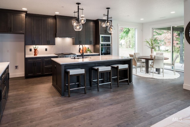 7755 W Flathead Lake St, Eagle, ID 83616 - kitchen with stainless steel oven, light countertops, a sink, a kitchen island with sink, and dark wood-style floors