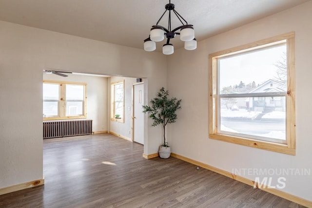 unfurnished room featuring dark wood-style floors, radiator, a chandelier, and baseboards