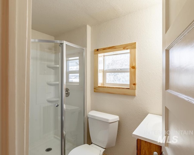 full bath featuring a textured wall, a stall shower, vanity, and toilet