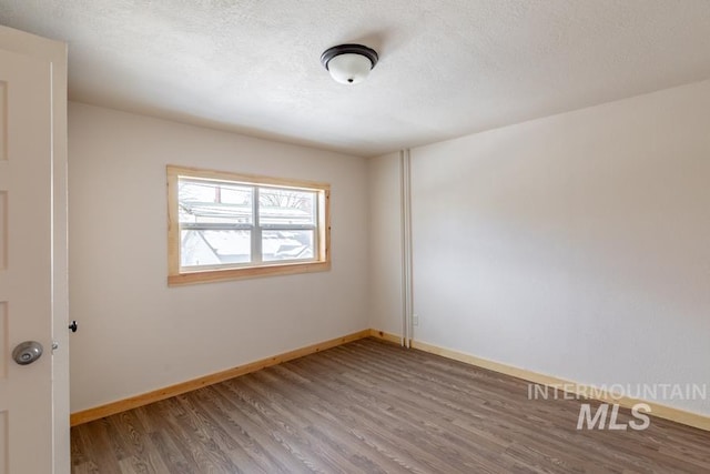 unfurnished room featuring a textured ceiling, baseboards, and wood finished floors