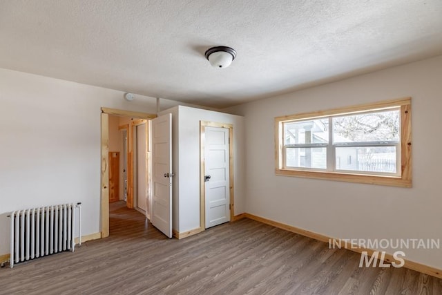 spare room featuring radiator heating unit, a textured ceiling, baseboards, and wood finished floors