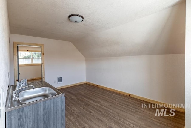 bonus room with dark wood finished floors, lofted ceiling, a sink, a textured ceiling, and baseboards