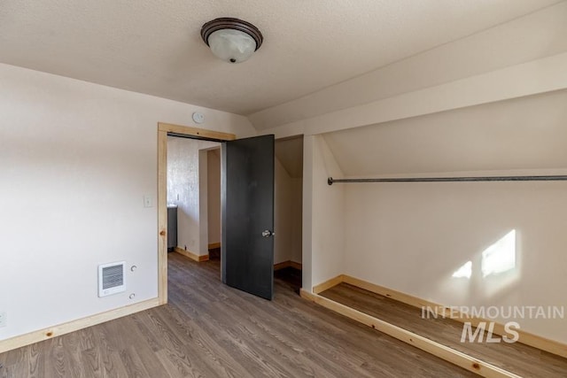 empty room with a textured ceiling, wood finished floors, visible vents, baseboards, and vaulted ceiling