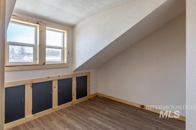 bonus room with lofted ceiling, dark wood-style flooring, a textured ceiling, and baseboards