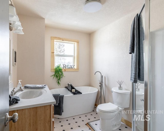 bathroom featuring a textured ceiling, toilet, vanity, a freestanding bath, and tile patterned floors