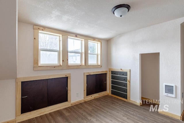 unfurnished room with a textured ceiling, heating unit, and wood finished floors