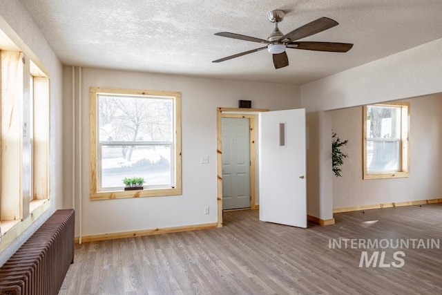 empty room with light wood finished floors, radiator heating unit, a ceiling fan, a textured ceiling, and baseboards