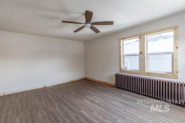 unfurnished room featuring radiator heating unit, a ceiling fan, a textured ceiling, wood finished floors, and baseboards