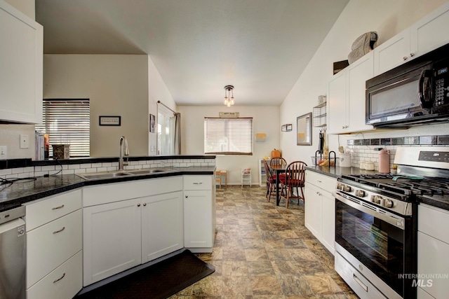 kitchen with kitchen peninsula, white cabinets, appliances with stainless steel finishes, vaulted ceiling, and sink