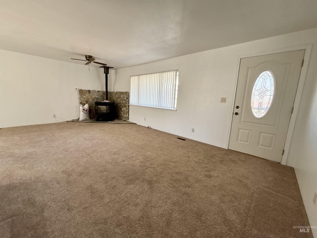 unfurnished living room featuring ceiling fan, a healthy amount of sunlight, carpet, and a wood stove