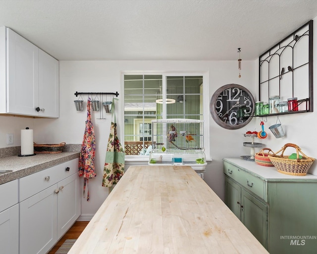 kitchen with a textured ceiling, butcher block countertops, and white cabinetry