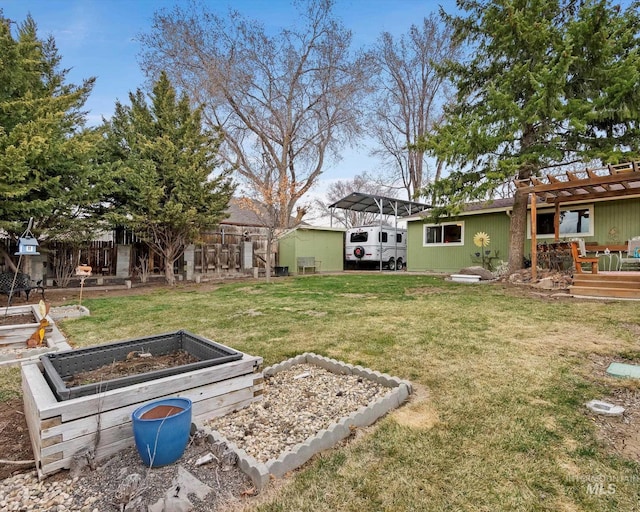 view of yard with a deck, a vegetable garden, a detached carport, and fence