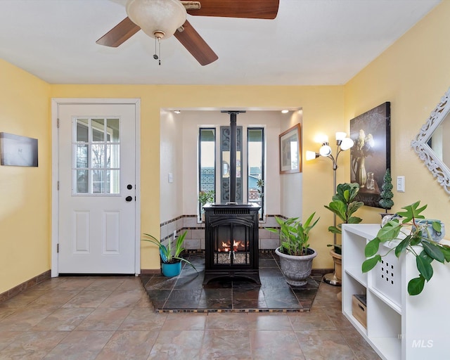 foyer entrance with a wealth of natural light, baseboards, ceiling fan, and a wood stove