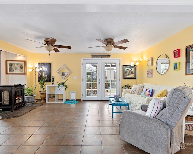 living room featuring a ceiling fan, a wood stove, tile patterned flooring, french doors, and a textured ceiling