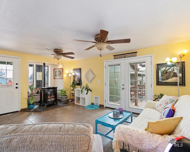 living room featuring tile patterned floors, baseboards, ceiling fan, and a wood stove