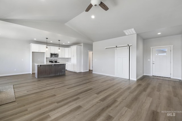 unfurnished living room featuring ceiling fan, sink, a barn door, vaulted ceiling, and hardwood / wood-style flooring