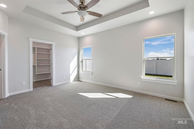 unfurnished bedroom featuring light carpet, a walk in closet, a raised ceiling, ceiling fan, and a closet