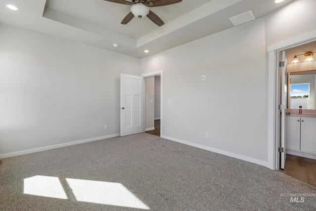 unfurnished bedroom featuring a raised ceiling, carpet floors, ensuite bath, and ceiling fan