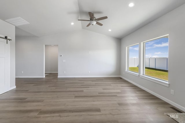 empty room with ceiling fan, a barn door, light hardwood / wood-style floors, and vaulted ceiling