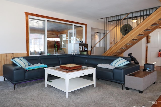 living room featuring wainscoting, carpet flooring, wooden walls, and stairs