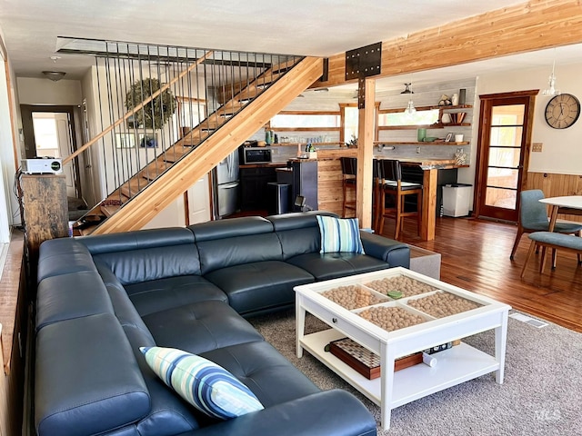 living room featuring visible vents, wainscoting, stairway, dark wood-type flooring, and wood walls