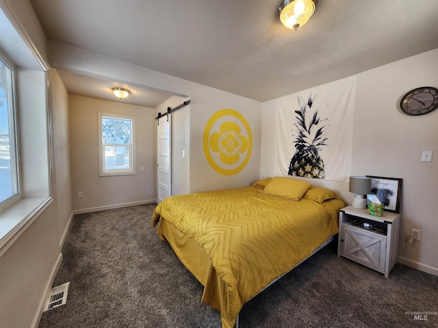 bedroom with a barn door, dark carpet, visible vents, and baseboards