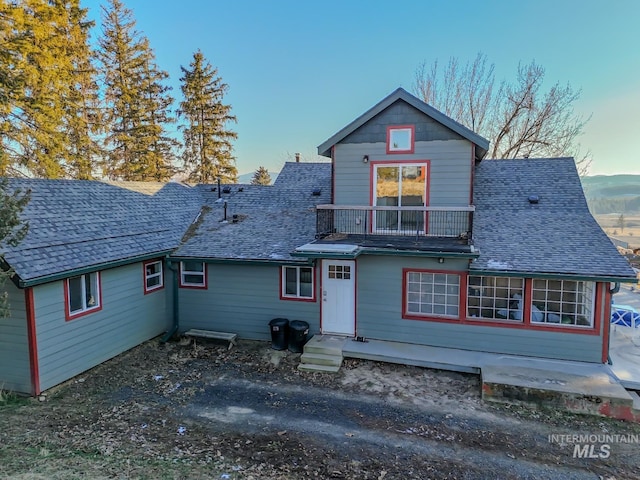 view of front facade featuring a shingled roof, entry steps, and a balcony