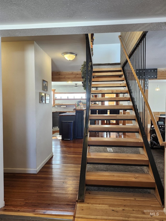 staircase with a textured ceiling, baseboards, and wood finished floors