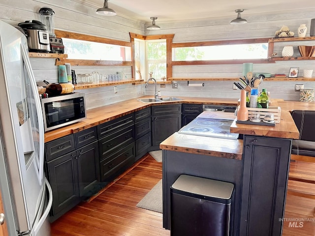 kitchen with butcher block counters, stainless steel microwave, hanging light fixtures, refrigerator with ice dispenser, and a sink