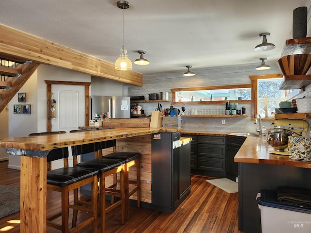 kitchen featuring dark wood-style flooring, dark cabinetry, a sink, butcher block countertops, and stainless steel fridge