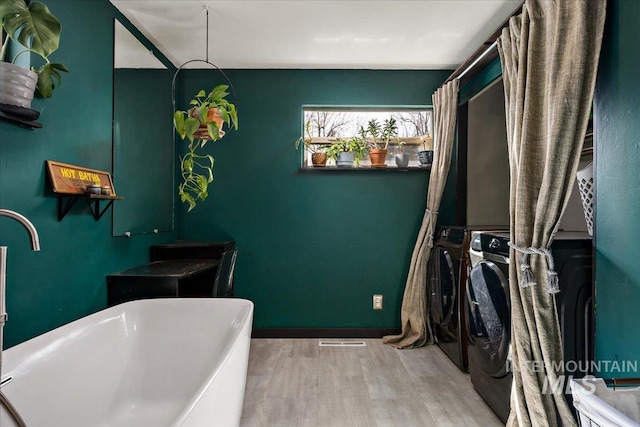 bathroom with baseboards, a freestanding bath, wood finished floors, and washer and clothes dryer