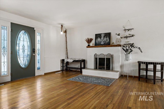 foyer entrance with a fireplace with raised hearth, baseboards, and wood finished floors